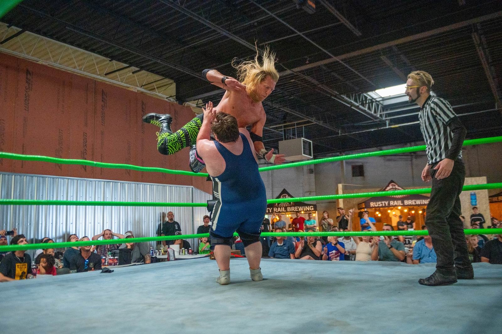 A wrestler is lifted in the air during a SlamFest Live match as the crowd watches